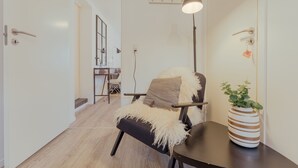 A modern interior with a wooden floor, a black armchair with a beige throw, a lamp, and a striped vase with a plant.