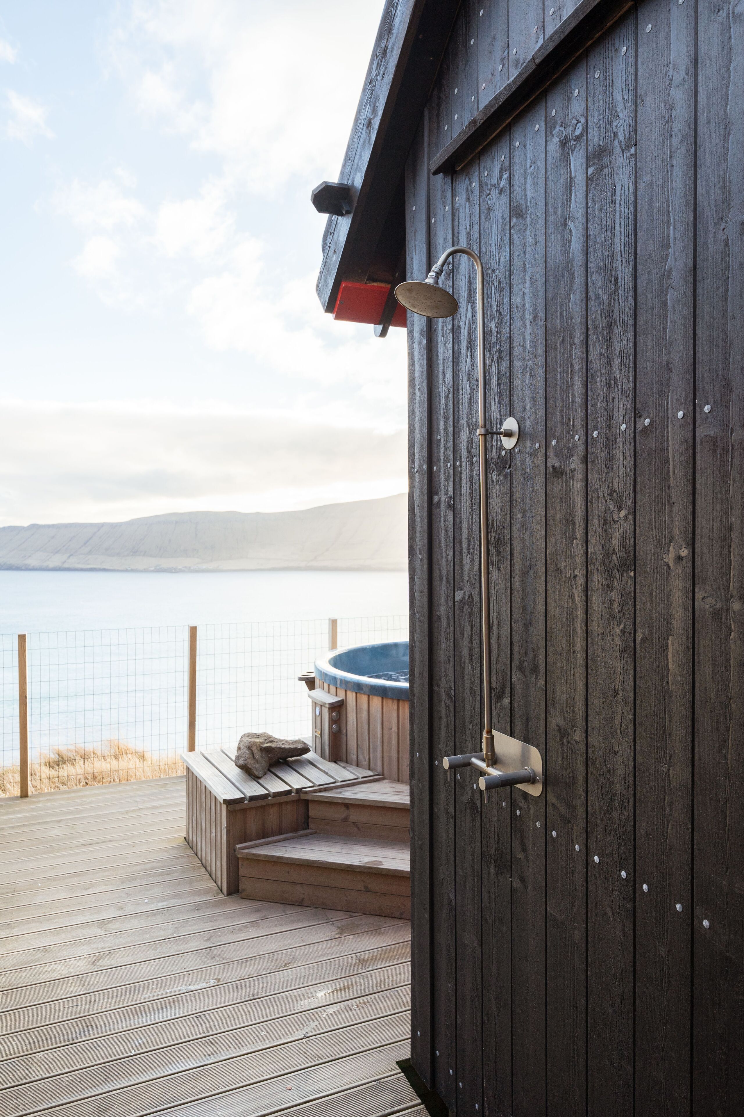 Eine Holzterrasse mit Whirlpool und Blick auf das Wasser.