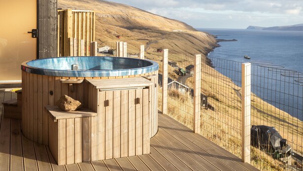 Une terrasse en bois avec un jacuzzi et vue sur la côte.