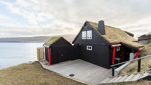 Un bâtiment en bois noir, doté d’un toit de chaume, d’une terrasse en bois et offrant une vue sur l’eau.