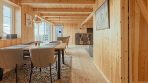 Un intérieur en bois comprenant un coin repas, des chaises, une table, un tapis et une bibliothèque.