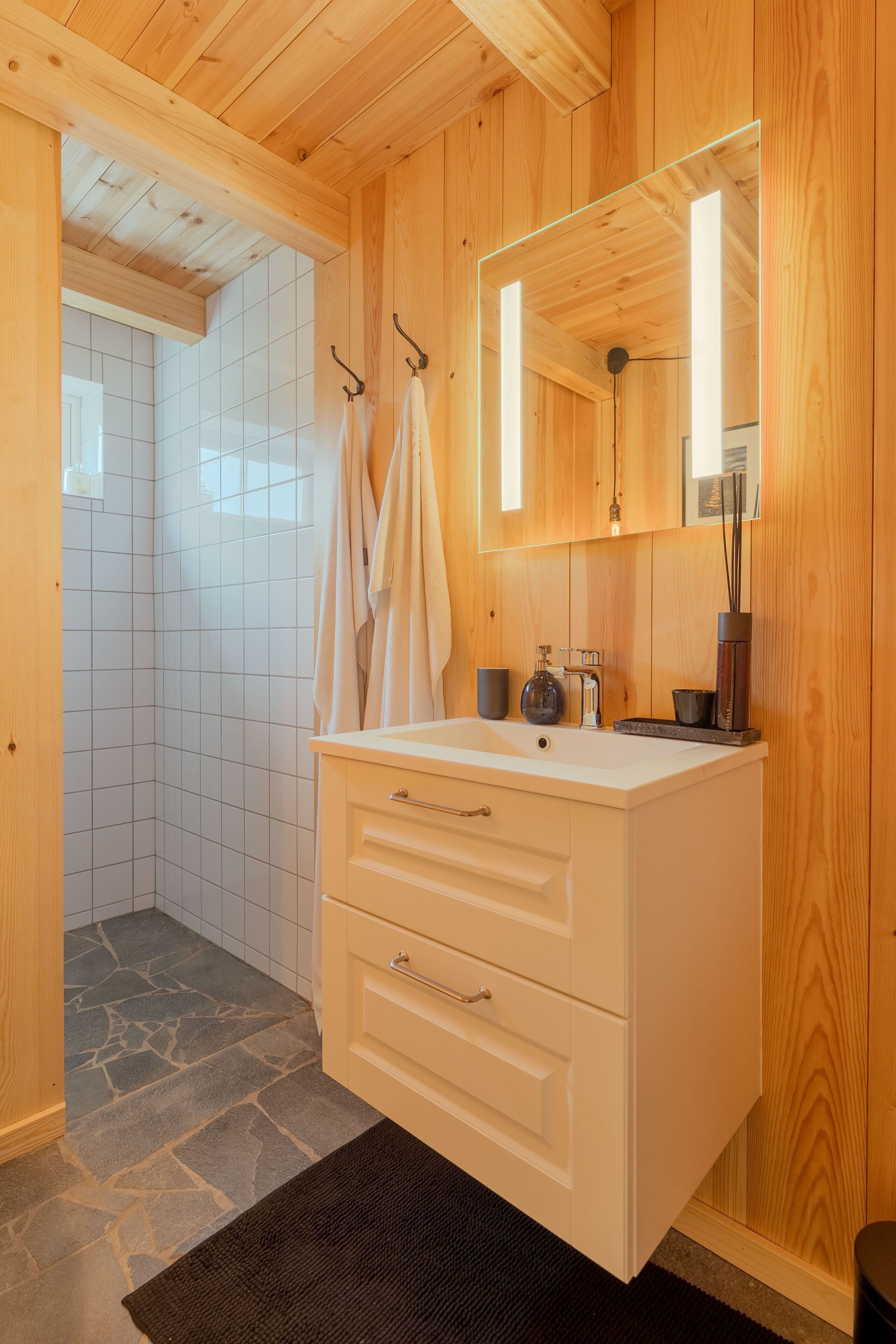 Ein Badezimmer mit Holzvertäfelung, einem weißen Waschtisch, einem Spiegel und einer Duschkabine.