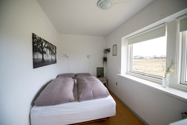 Un dormitorio con cama, una ventana que da a un campo, un espejo en la pared y un cuadro.