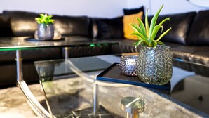 A modern living room with a glass coffee table, a black leather sofa, and a small potted plant. - Old Sherrif'S House | Family Friendly | Beach (Sandur)