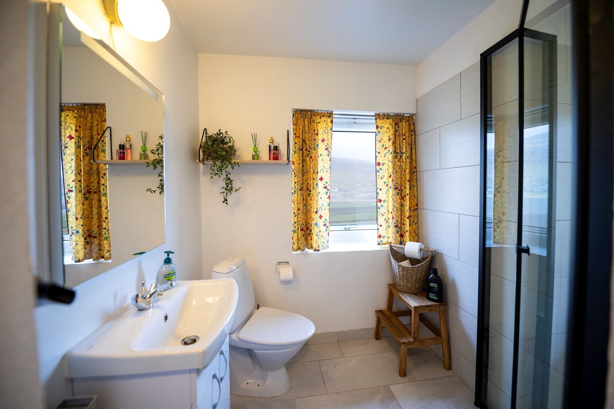 A bathroom with a white sink, toilet, and a window with floral curtains.