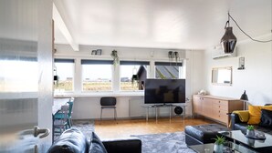 A modern living room with a large TV, comfortable seating, and large windows offering a view of the countryside. - Old Sherrif'S House | Family Friendly | Beach (Sandur)