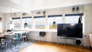 A modern living room with a large TV, a dining area with chairs, and a view of the sea through large windows. - Old Sherrif'S House | Family Friendly | Beach (Sandur)