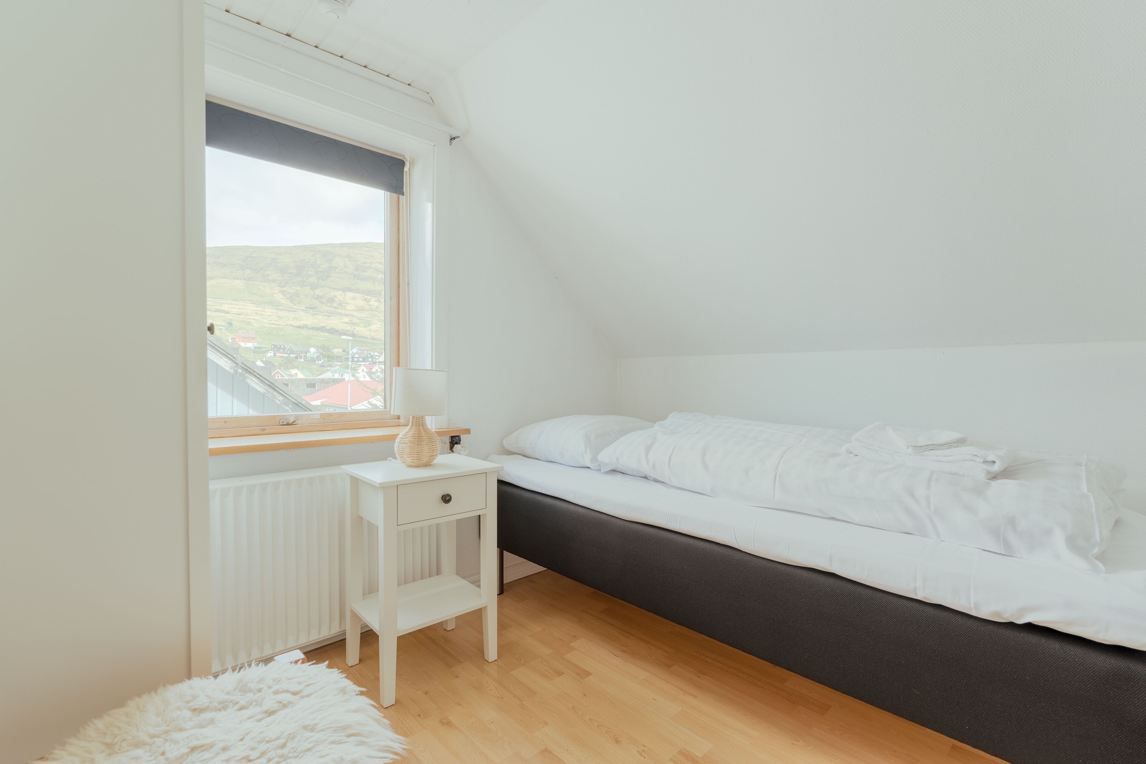 Un dormitorio con cama, mesita de noche, lámpara y vista a un paisaje a través de una ventana.