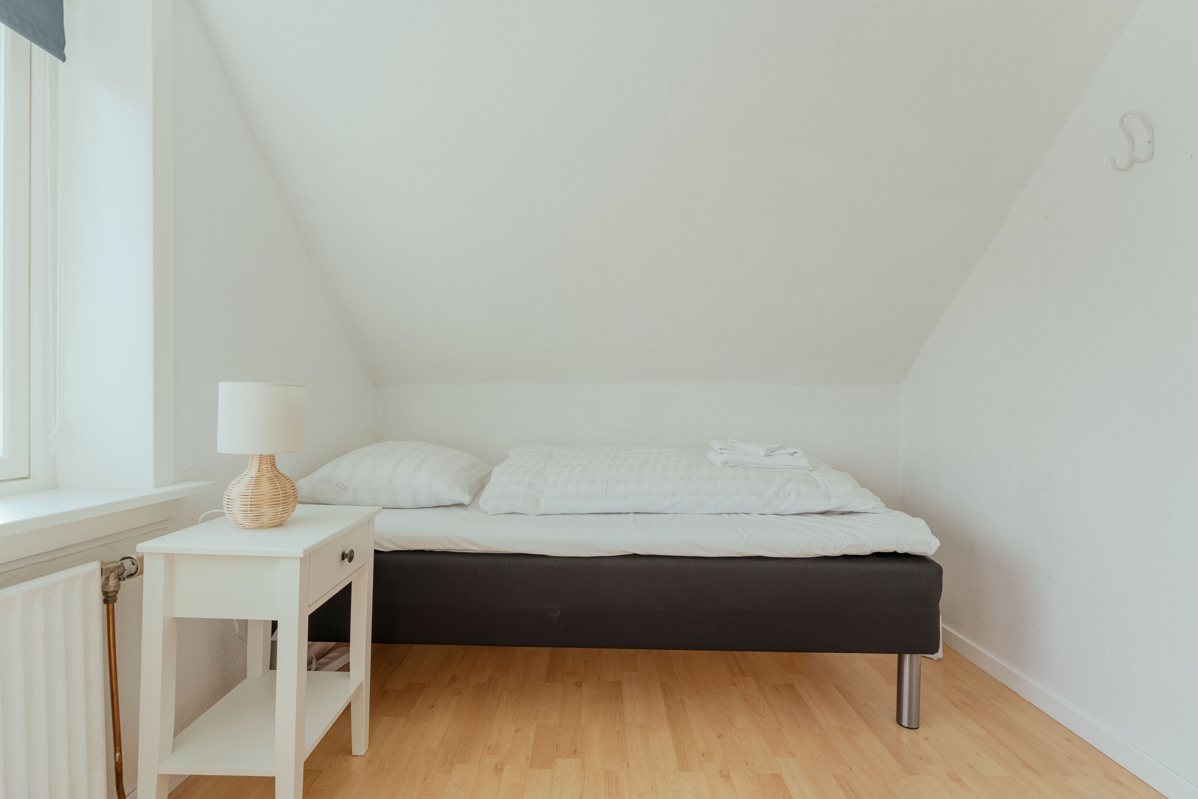 A small, neatly arranged bedroom with a single bed, a bedside table with a lamp, and a radiator.