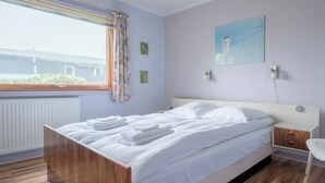 A neatly made bed with white linens and towels, a wooden headboard, a nightstand with a lamp, and a window with curtains. - Charming 2-Bedroom Home | 20 Min Walk To City Centre (Tórshavn)