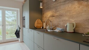 A modern kitchen with a large window, a built-in oven, a sink, and a kettle on the counter. - Charming Central Tórshavn Retreat - 2Br Apartment (Tórshavn)