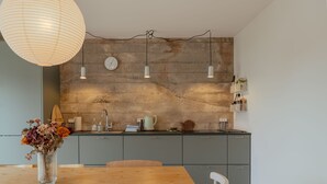 A modern kitchen with a concrete backsplash, pendant lights, and a wooden dining table. - Charming Central Tórshavn Retreat - 2Br Apartment (Tórshavn)