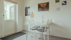 Un comedor con una mesa blanca y cuatro sillas, una tabla de cortar de madera, y obras de arte en la pared.