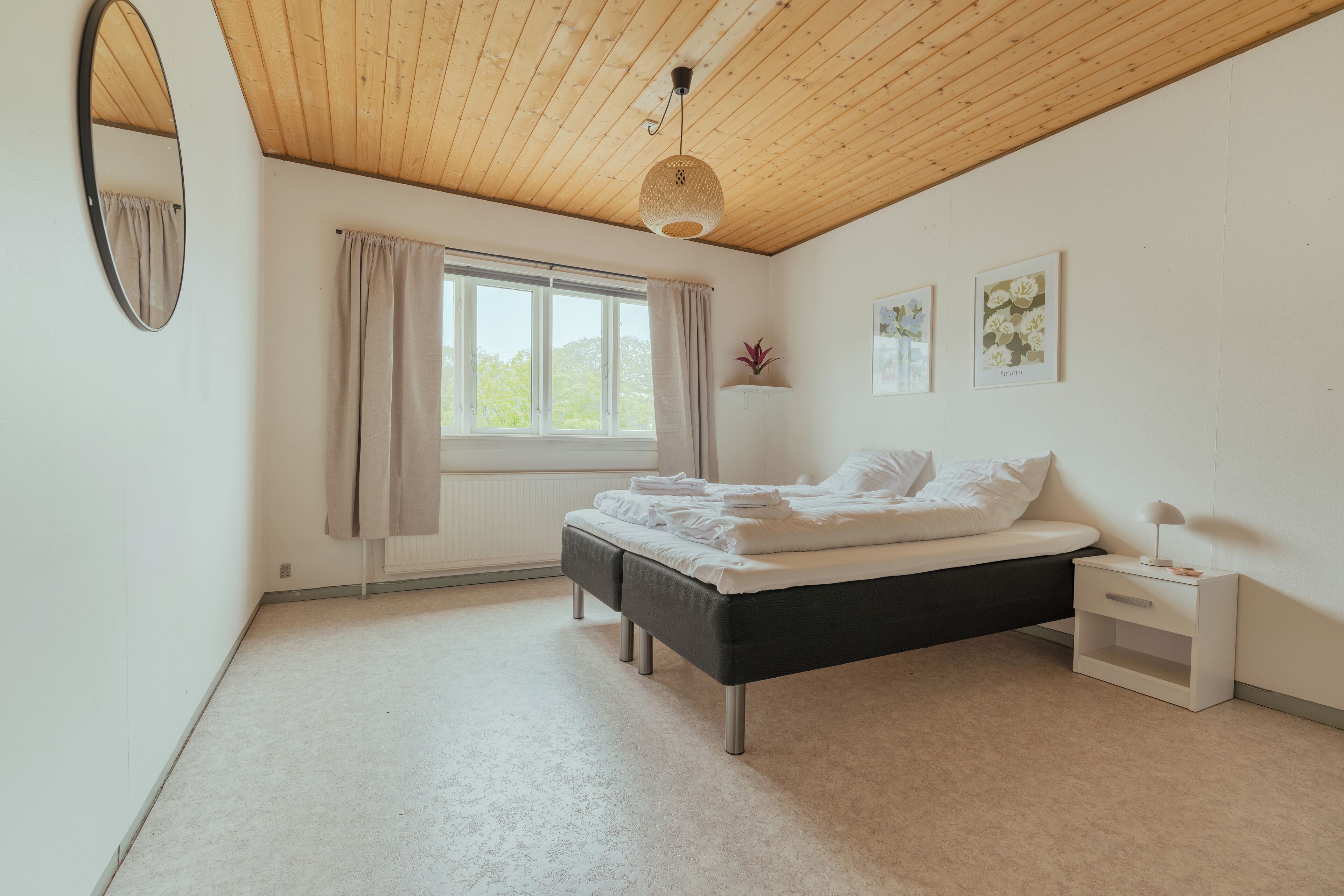 Un dormitorio con cama, mesita de noche, ventana y espejo.