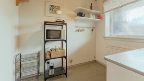 Una cocina con encimera blanca, una estantería de metal negro y repisas con utensilios de cocina.