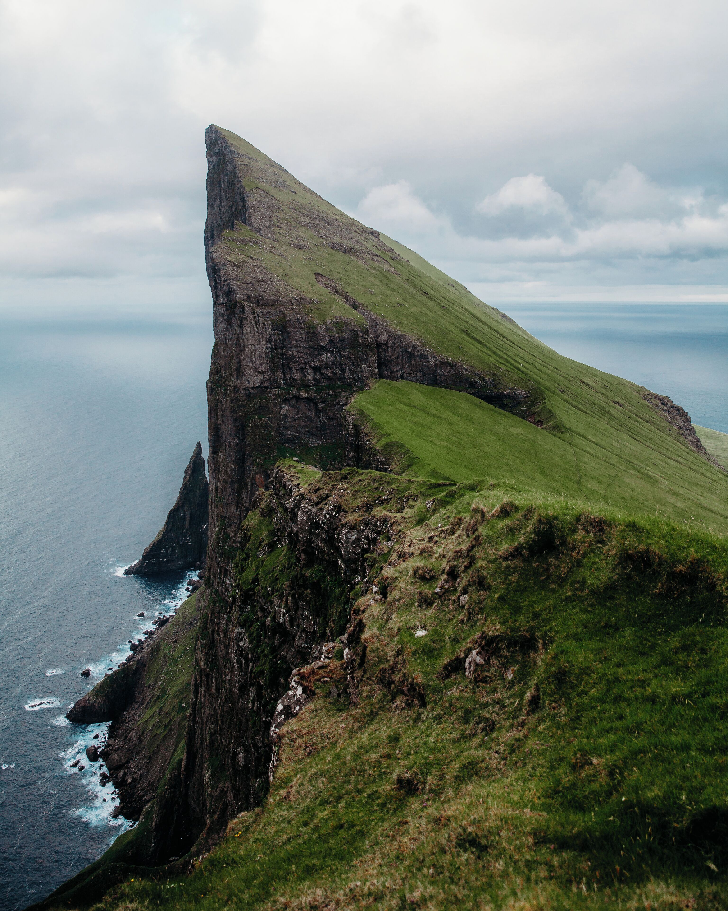 A rugged cliff with a grassy slope overlooking the sea.