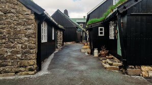 Una calle estrecha bordeada de edificios tradicionales de piedra y madera, algunos con techos de hierba.