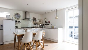 Una cocina moderna con armarios blancos, una mesa de comedor de madera y sillas. Hay un reloj en la pared y una ventana que proporciona luz natural.