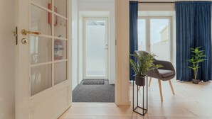 Ein modernes Interieur mit Holzboden, einer Glastür, die auf einen Balkon führt, einem schwarzen Stuhl mit Topfpflanze und einem blauen Vorhang.