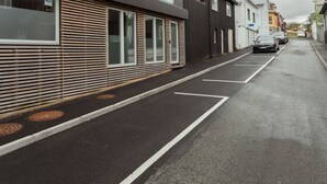 Straßenansicht mit modernen Gebäuden, einer klaren Fahrbahn und geparkten Autos.