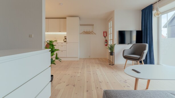 Ein modernes Wohnzimmer mit einem Flachbildfernseher, einem grauen Sessel und einem kleinen weißen Tisch.