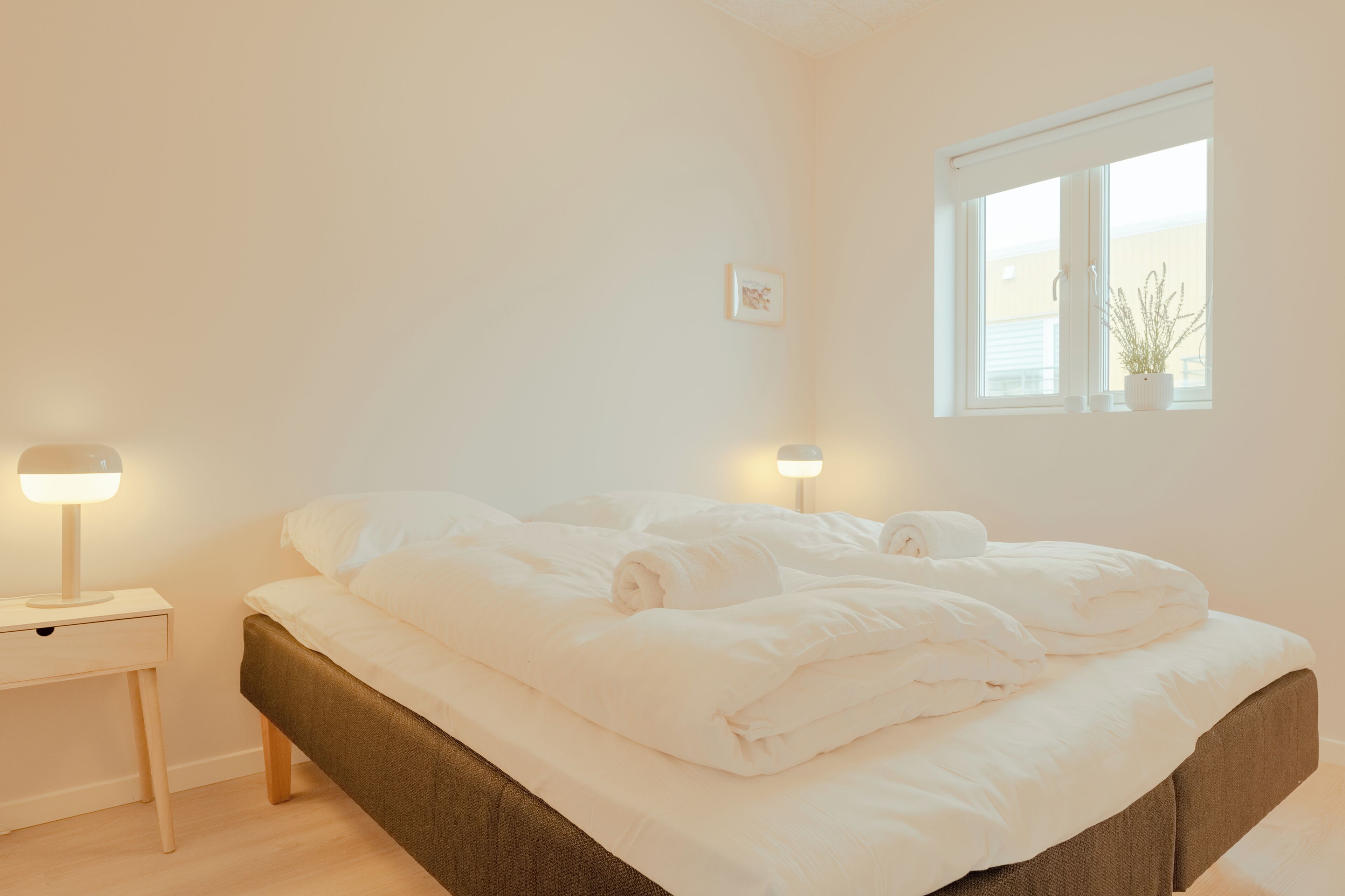 A bedroom with a bed, bedside tables, a window, and a wall-mounted picture.