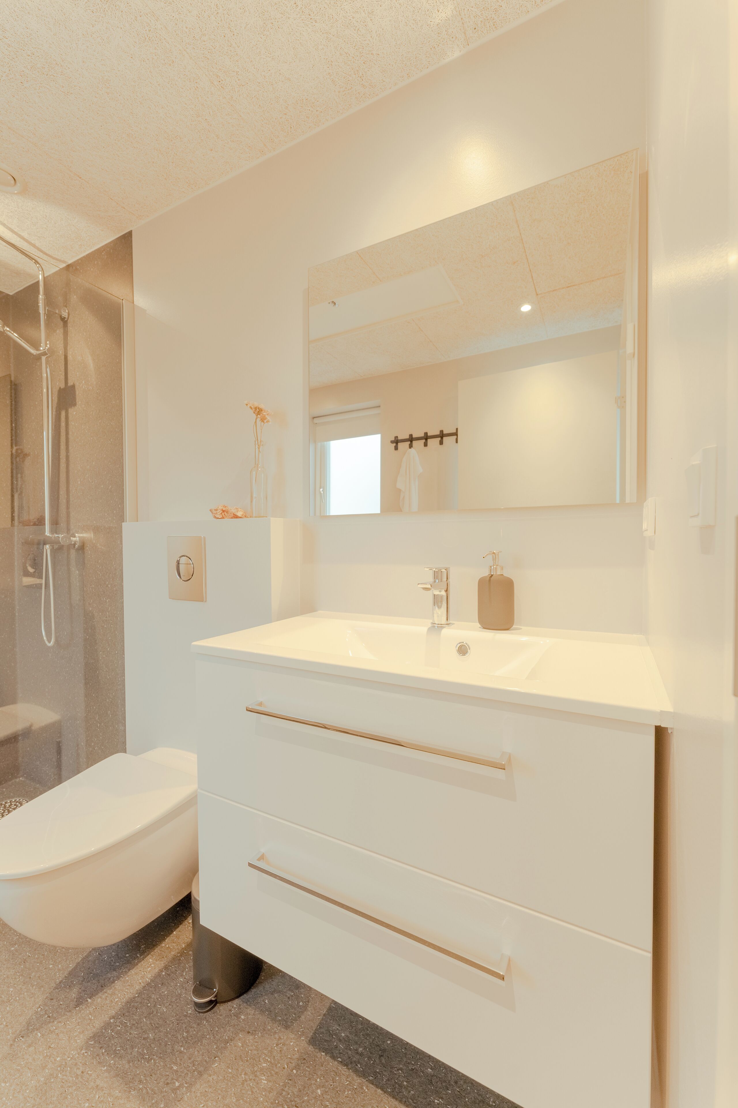 Een moderne badkamer met een wit wastafelmeubel, een douchecabine met glazen wanden en een toilet.