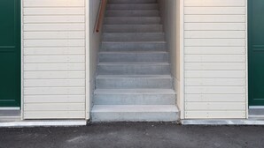 A staircase leading to a building entrance with two exterior wall-mounted lights and a green door on the left. - Charming Artistic Retreat | Panoramic View (Hoyvík)