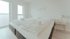 A minimalist bedroom with a large bed, a bedside table, and a window. - Charming Artistic Retreat | Panoramic View (Hoyvík)