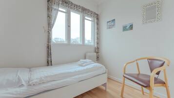 A room with a single bed, a chair, a radiator, and two framed pictures on the wall.