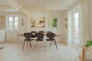 Un comedor con una mesa de madera y cuatro sillas, una lámpara colgante y obras de arte en las paredes.