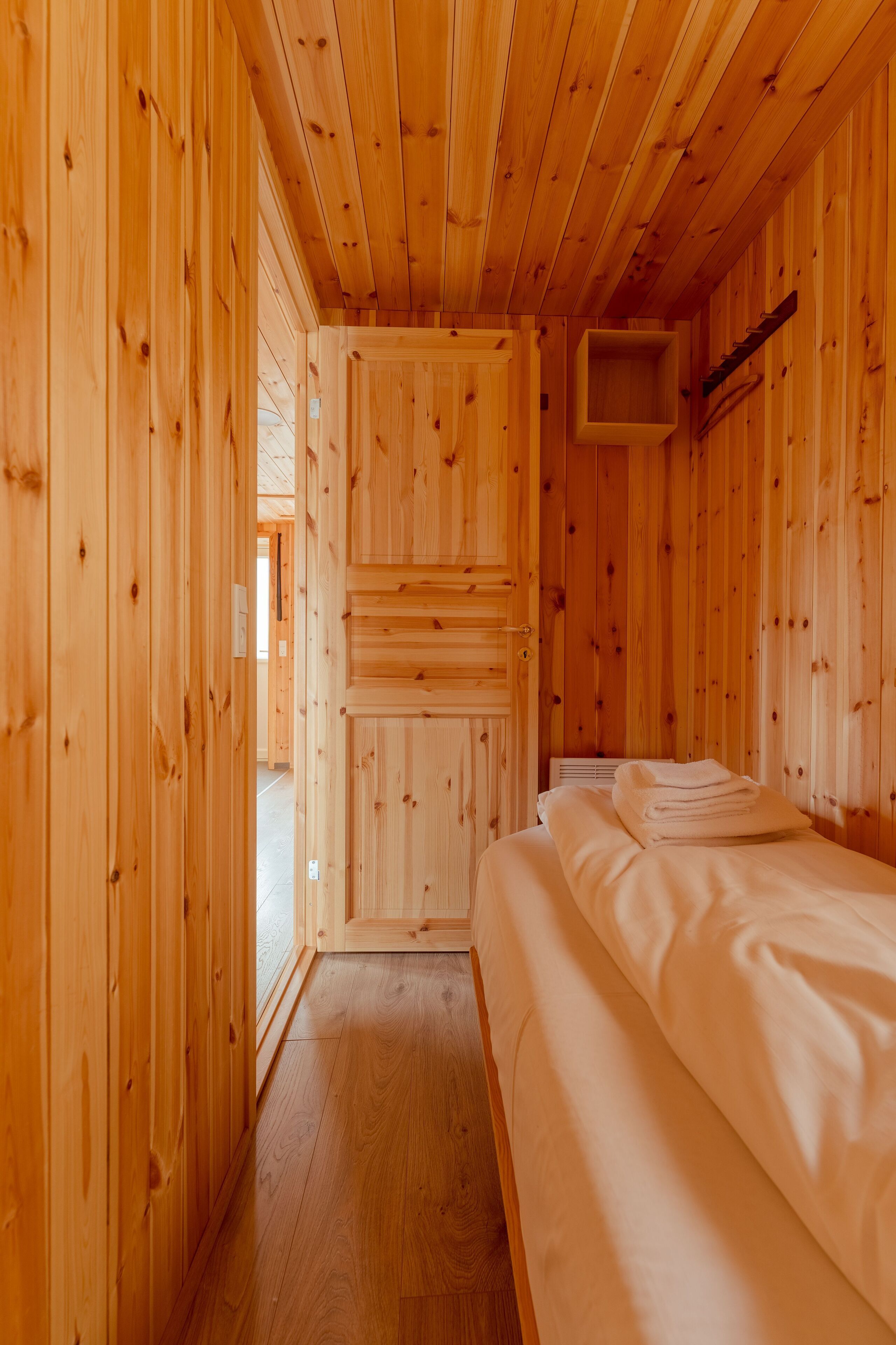 A wooden cabin room with a bed, a small window, and a door leading outside.