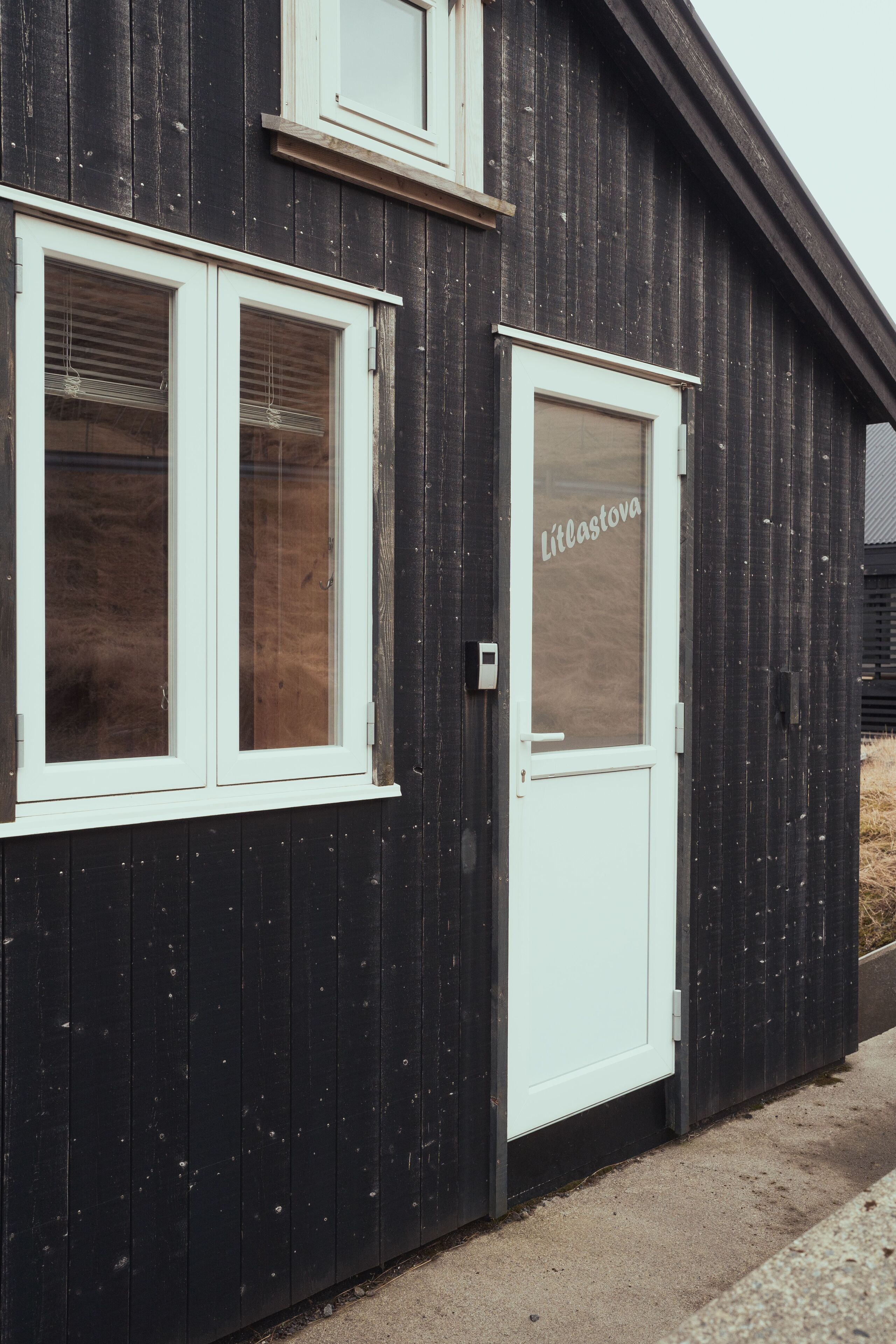 A black wooden building with two windows and a door.