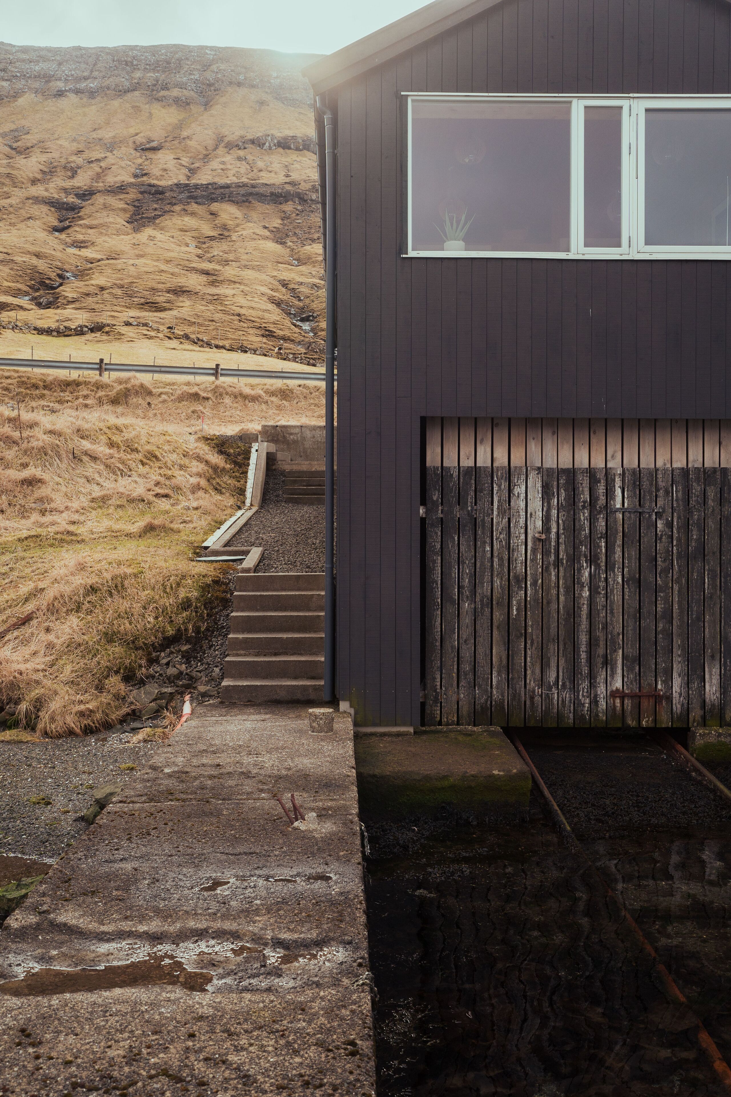 A building with a dark exterior, a wooden fence, and a concrete staircase leading to a garage.