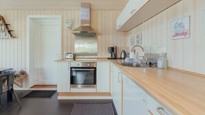 A compact kitchen with wooden paneling, a built-in oven, a stainless steel range hood, and a wooden countertop. - Charming Cottage In Tranquil Village - Hot Tub (Skalavik)