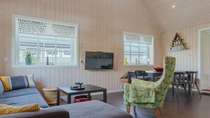 A spacious living area with a high ceiling, wooden walls, a sofa, a chair, a dining table, and a TV. - Charming Cottage In Tranquil Village - Hot Tub (Skalavik)
