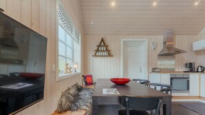 A modern kitchen with wooden walls, a central island, and a dining area with chairs and a red bowl. - Charming Cottage In Tranquil Village - Hot Tub (Skalavik)