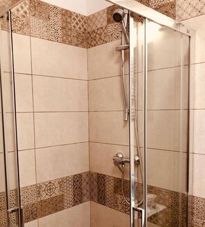 A shower with a glass door, patterned tiles, and a handheld showerhead. - Joy City Stay Paris 4 3 (Timișoara)