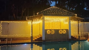 Un pabellón junto a la piscina con luces colgantes, una escalera y aros inflables.