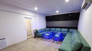 Una sala de estar con un sofá verde, dos mesitas cúbicas azules y una alfombra estampada.