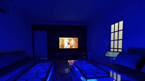 Una habitación con una televisión grande, un sofá y una mesa con superficie iluminada en azul.