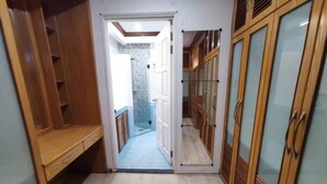 Un corridoio stretto con armadietti in legno e una panca a sinistra, che conduce a un bagno con doccia e parete piastrellata.