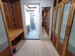 A narrow hallway with wooden cabinets and a bench on the left, leading to a bathroom with a shower and a tiled wall.