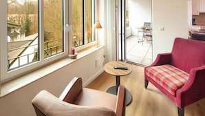 Ein modernes Wohnzimmer mit großem Fenster, einem roten Sessel, einem beigen Sofa und einem kleinen runden Tisch mit Fernbedienung.