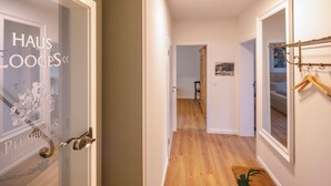 Ein Korridor mit Holzboden, einer Tür mit Fensterglas, auf der 'HAUS LOOGES' und 'PLUMBHOMS' stehen, und einem Kleiderständer mit Kleiderbügeln.