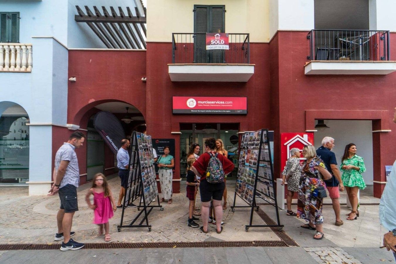 Un edificio con fachada roja, un cartel de 'SOLD' y una dirección web para servicios de bienes raíces.
