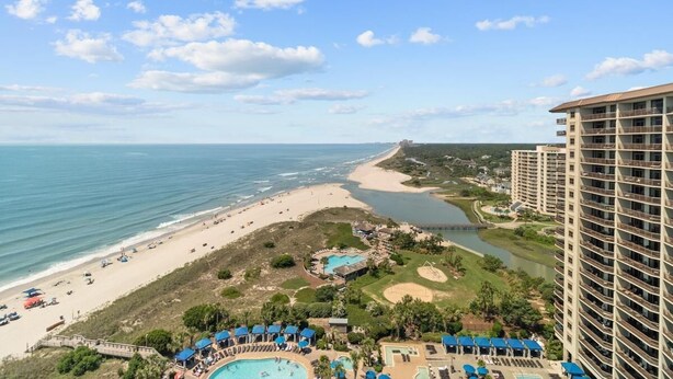 Een resort met een strand, zwembad en hoge gebouwen.