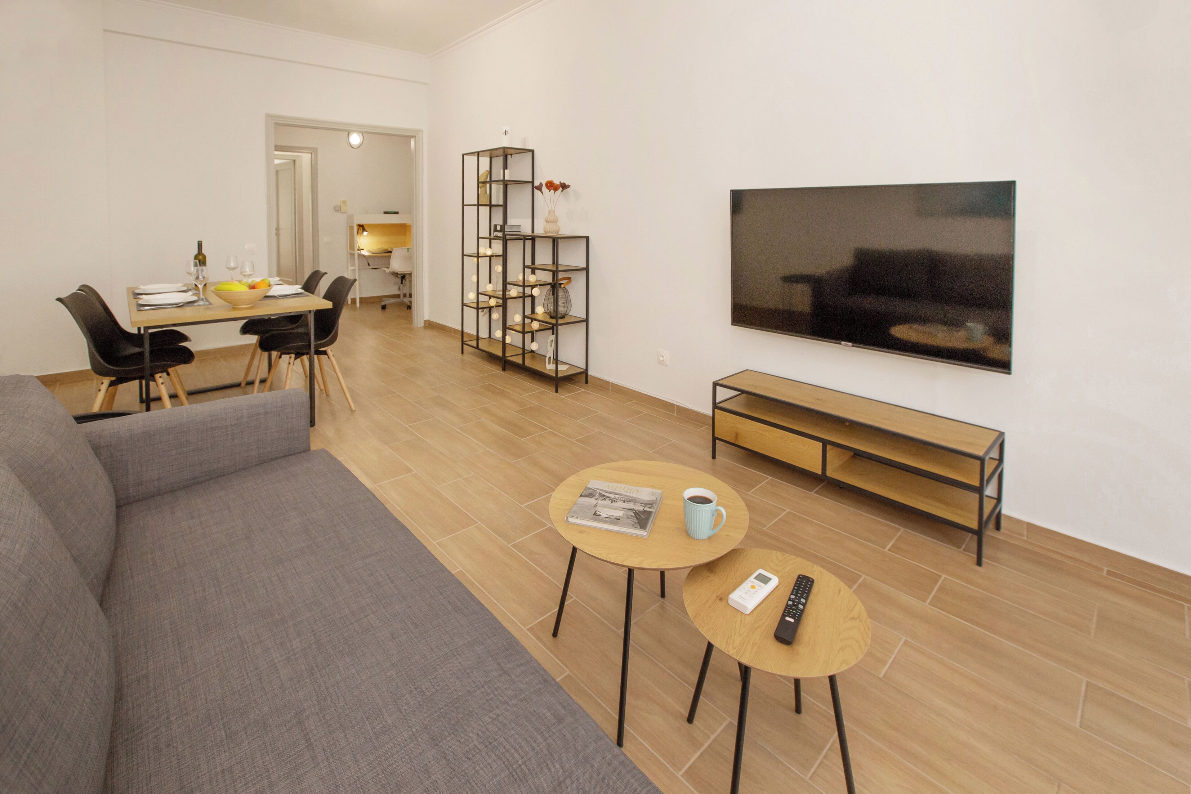 Un salon moderne avec un canapé gris, une table basse, un téléviseur et un coin repas comprenant des chaises et une table.