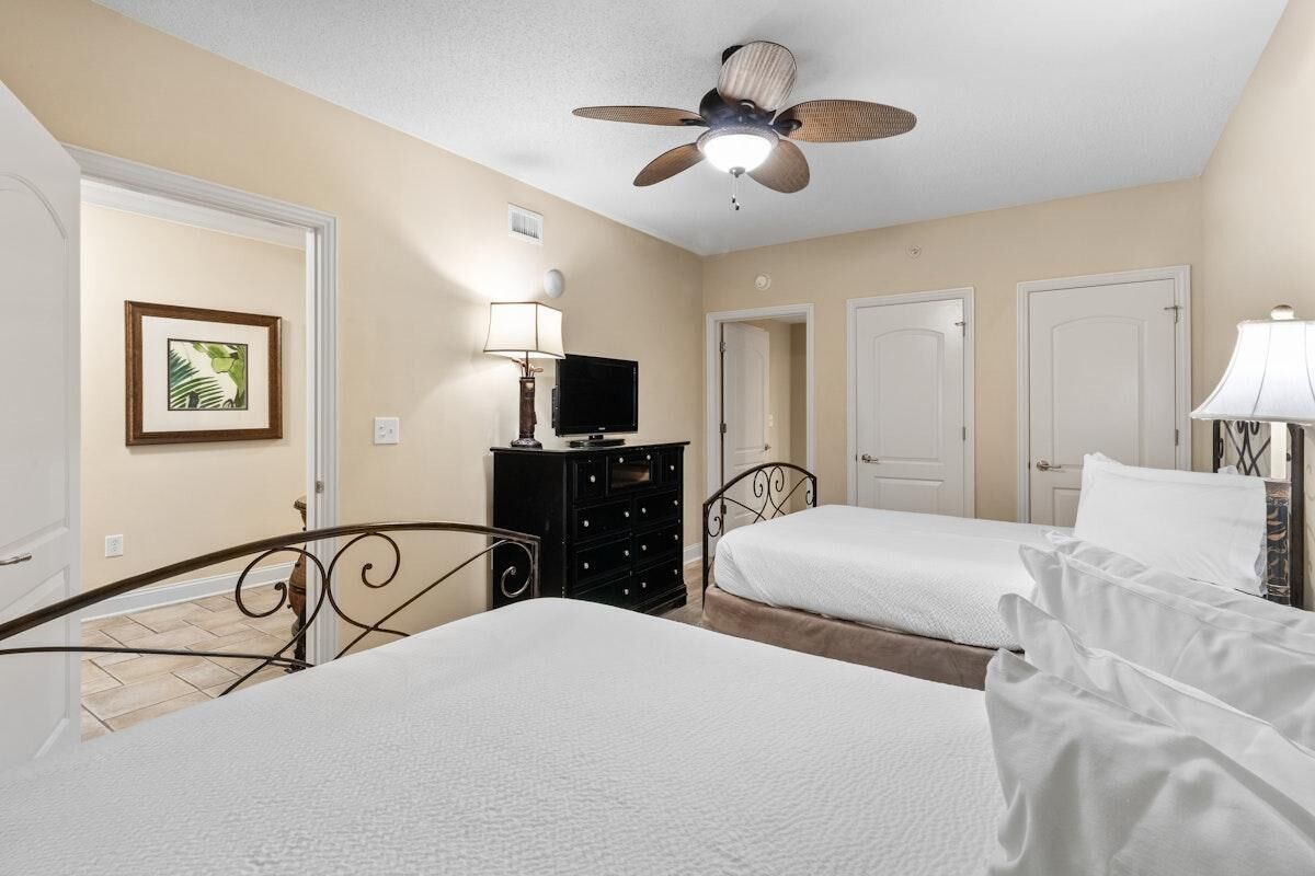 A bedroom with two beds, a ceiling fan, a TV, and a dresser.