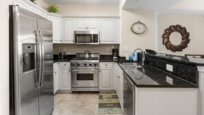 A modern kitchen with stainless steel appliances, white cabinets, a black granite countertop, and a decorative wreath on the wall.